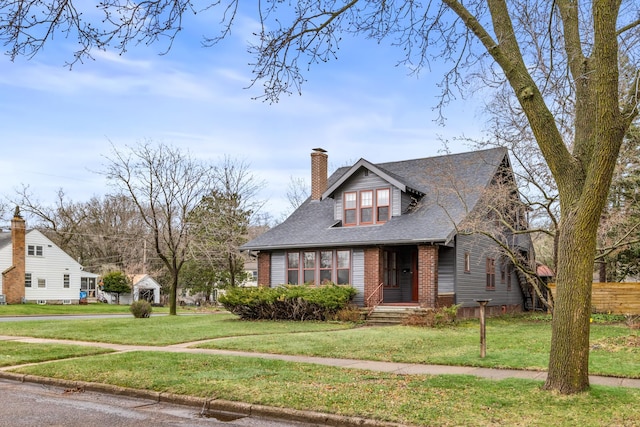 view of front facade with brick siding, a chimney, a front yard, and a shingled roof