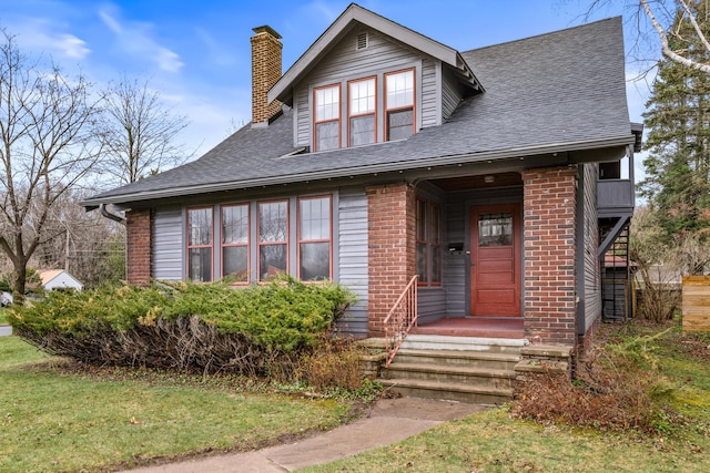view of front of home with brick siding, a chimney, roof with shingles, and a front lawn