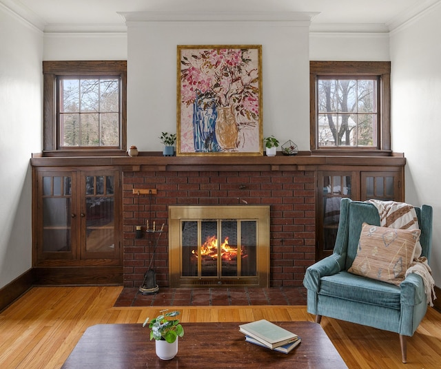 sitting room with a brick fireplace, wood finished floors, healthy amount of natural light, and ornamental molding