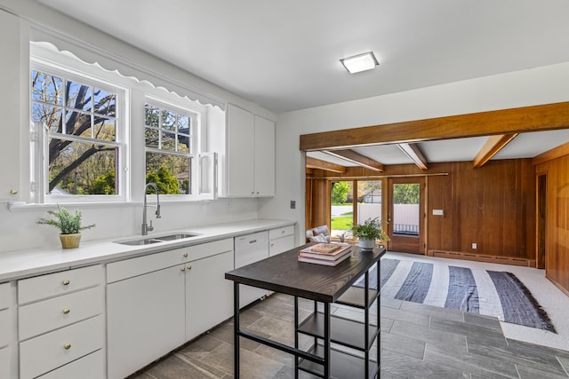 kitchen with a sink, baseboard heating, beam ceiling, light countertops, and dishwasher