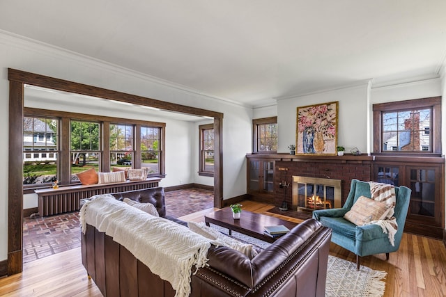 living area featuring baseboards, a fireplace, ornamental molding, and light wood-style flooring
