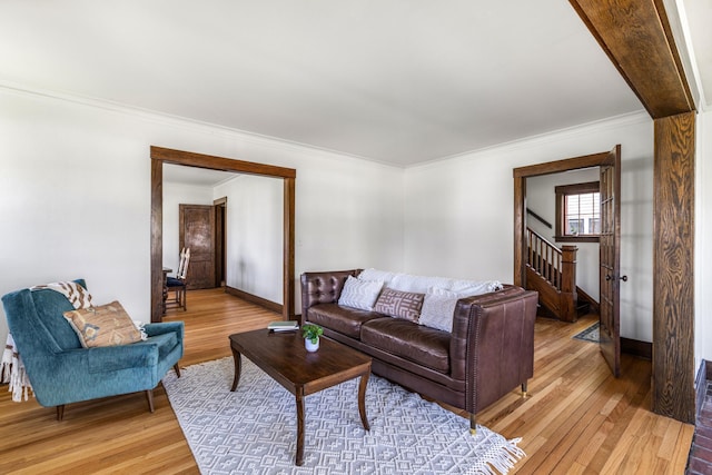 living room featuring light wood-type flooring, ornamental molding, stairs, and baseboards