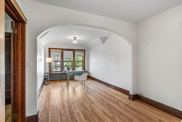 spare room with arched walkways, light wood-style flooring, baseboards, and radiator heating unit