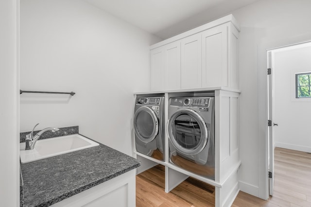 clothes washing area with cabinets, sink, light hardwood / wood-style floors, and washing machine and clothes dryer