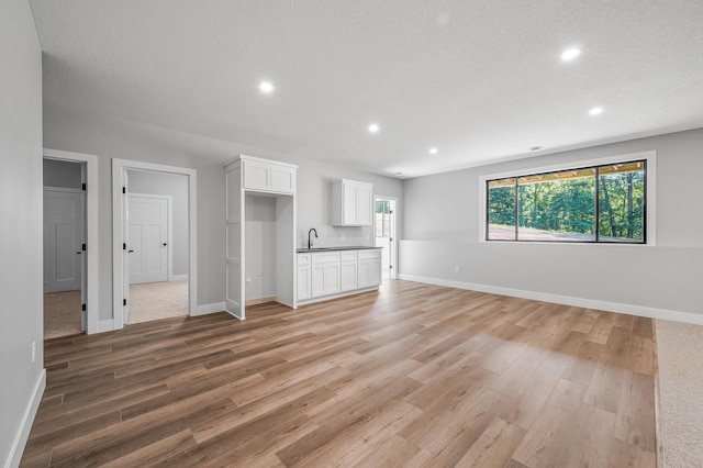 unfurnished living room featuring sink, a textured ceiling, and light wood-type flooring