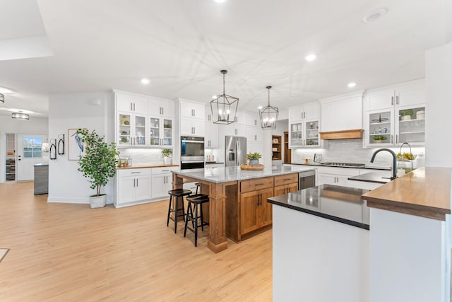 kitchen with white cabinetry, stainless steel appliances, light hardwood / wood-style flooring, pendant lighting, and a kitchen island