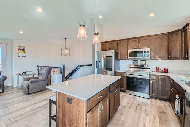 kitchen featuring light hardwood / wood-style flooring, decorative light fixtures, vaulted ceiling, a kitchen island, and appliances with stainless steel finishes