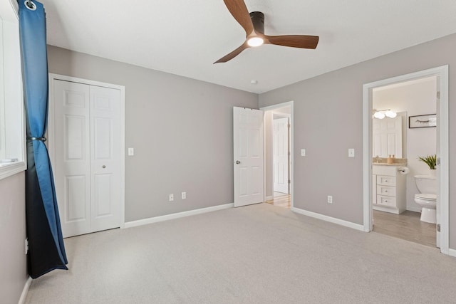 unfurnished bedroom with a closet, carpet, baseboards, ensuite bath, and ceiling fan