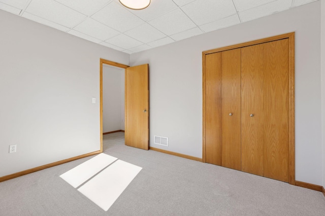 unfurnished bedroom featuring a closet, carpet, visible vents, a paneled ceiling, and baseboards
