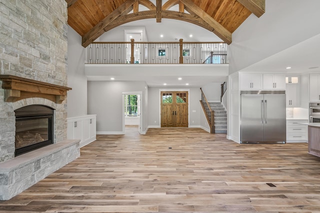 unfurnished living room with light hardwood / wood-style floors, high vaulted ceiling, and a stone fireplace