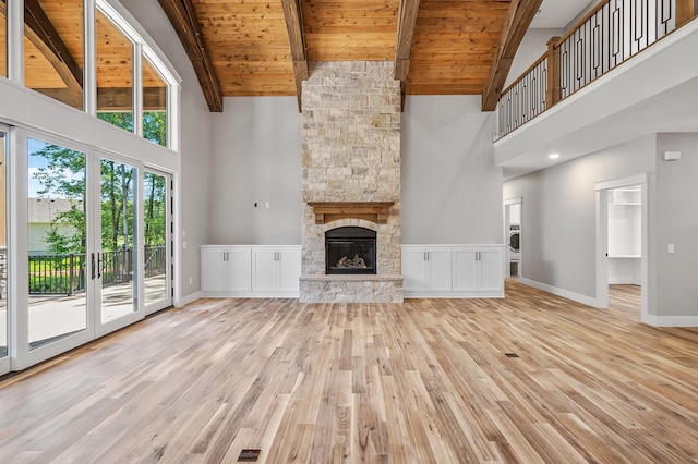 unfurnished living room featuring light hardwood / wood-style flooring, high vaulted ceiling, a stone fireplace, and wood ceiling