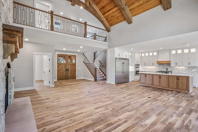 unfurnished living room with beamed ceiling, a fireplace, high vaulted ceiling, and light hardwood / wood-style flooring