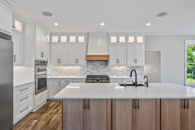 kitchen featuring white cabinets, premium range hood, and an island with sink