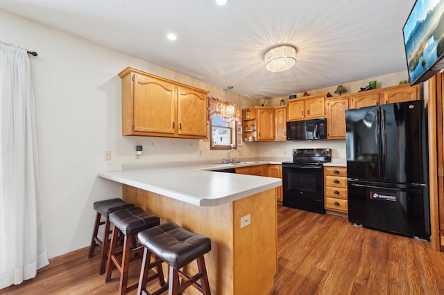 kitchen featuring black appliances, light hardwood / wood-style floors, a kitchen breakfast bar, sink, and kitchen peninsula