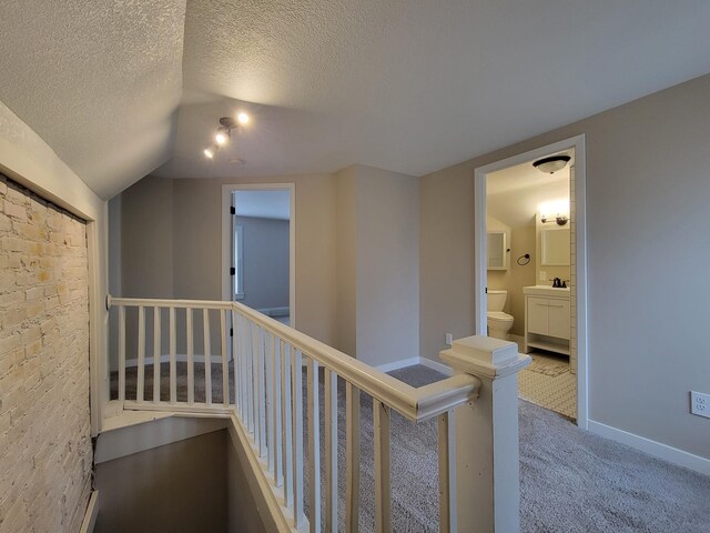 hall with a textured ceiling, sink, carpet, and lofted ceiling