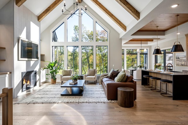 living room featuring hardwood / wood-style floors, an inviting chandelier, a fireplace, sink, and beam ceiling