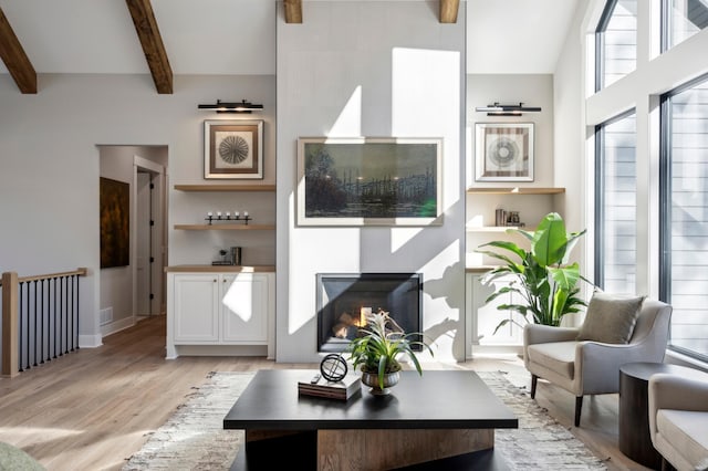 living room featuring beamed ceiling, a high ceiling, and light wood-type flooring