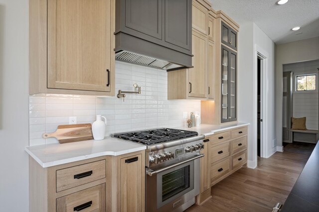 kitchen with light brown cabinetry, tasteful backsplash, wood-type flooring, high end stainless steel range, and a textured ceiling