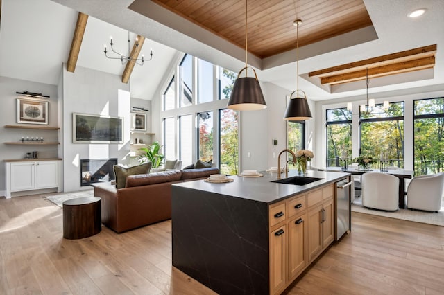 kitchen featuring sink, hanging light fixtures, a notable chandelier, a tray ceiling, and an island with sink