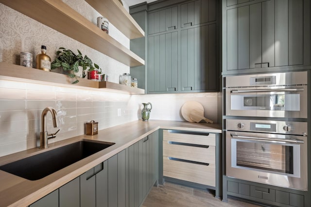 kitchen featuring tasteful backsplash, stainless steel double oven, light hardwood / wood-style floors, and sink