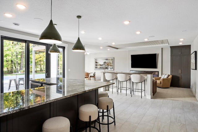 kitchen with a breakfast bar, pendant lighting, dark stone countertops, dark brown cabinets, and a textured ceiling