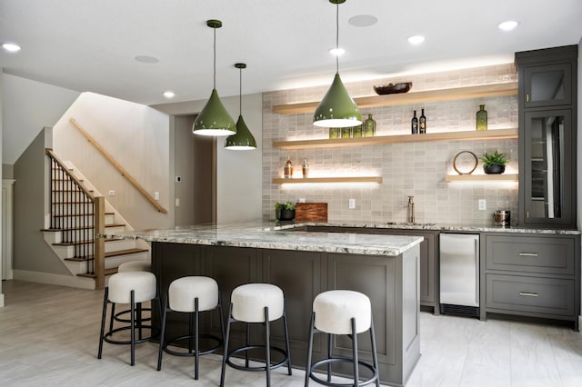 kitchen featuring decorative light fixtures, a breakfast bar area, stainless steel fridge, kitchen peninsula, and light stone countertops