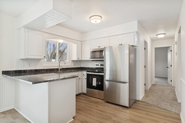 kitchen with sink, white cabinetry, appliances with stainless steel finishes, light hardwood / wood-style floors, and kitchen peninsula