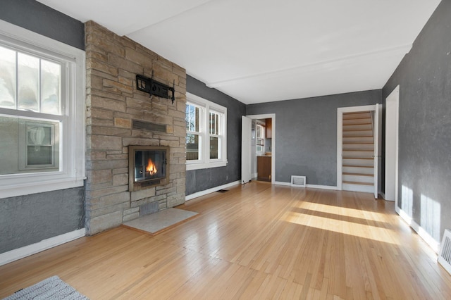 unfurnished living room with a stone fireplace and light hardwood / wood-style floors