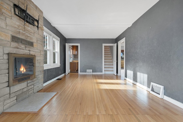 unfurnished living room featuring light wood-type flooring and a stone fireplace