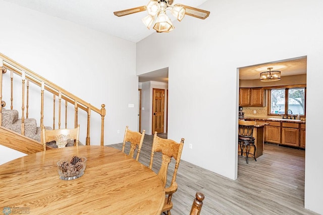 dining space featuring light wood-style floors, ceiling fan with notable chandelier, a towering ceiling, and stairs