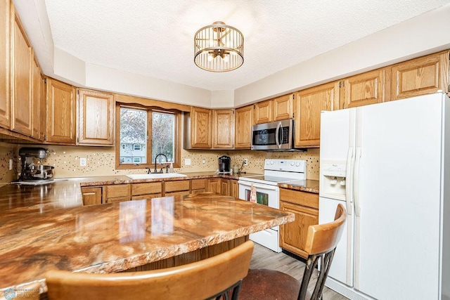 kitchen with a textured ceiling, a peninsula, white appliances, a breakfast bar, and a sink