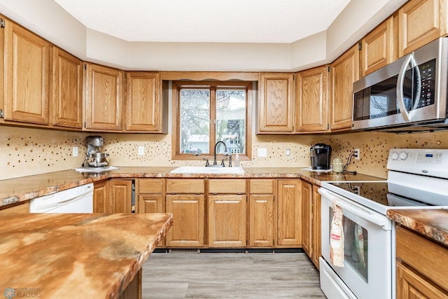 kitchen with light countertops, white appliances, backsplash, and a sink