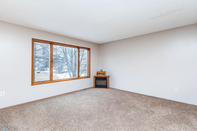 carpeted spare room featuring a glass covered fireplace