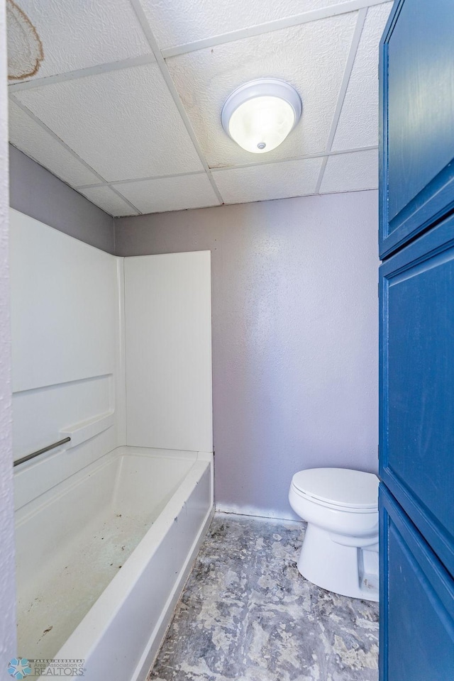 bathroom with a paneled ceiling, toilet, and a bath