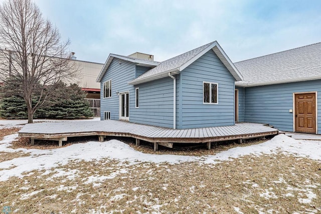 snow covered back of property with a deck and roof with shingles