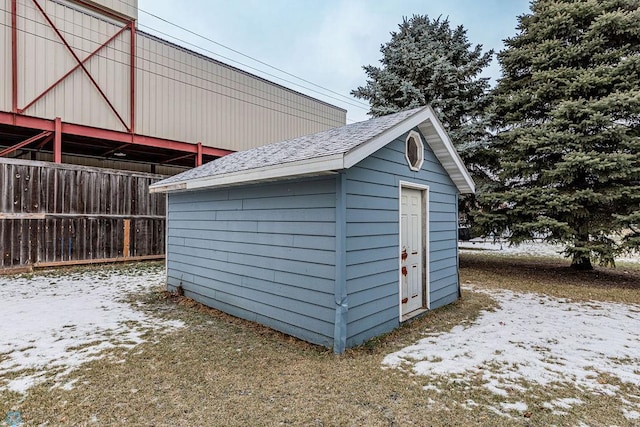 snow covered structure with an outbuilding, a storage shed, and fence