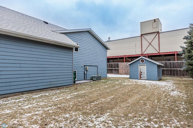 rear view of property featuring a storage unit, a shingled roof, fence, and an outbuilding