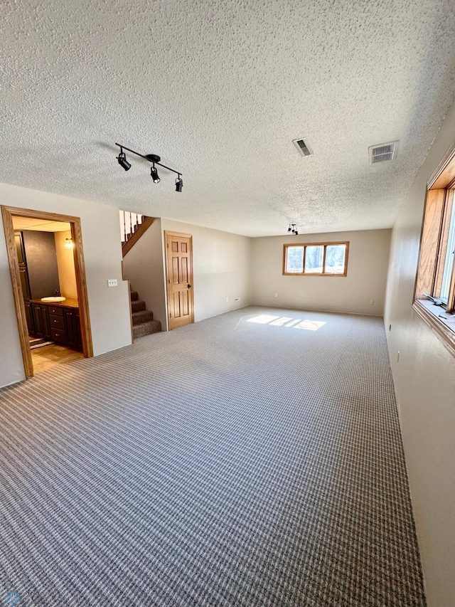 carpeted empty room with rail lighting, visible vents, stairway, and a textured ceiling