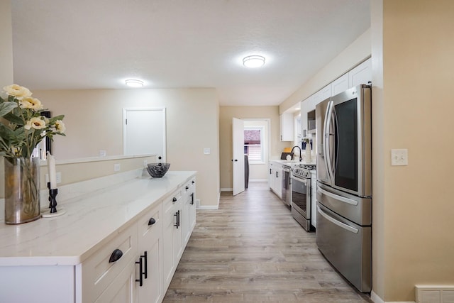 kitchen featuring white cabinets, sink, light hardwood / wood-style flooring, light stone countertops, and stainless steel appliances