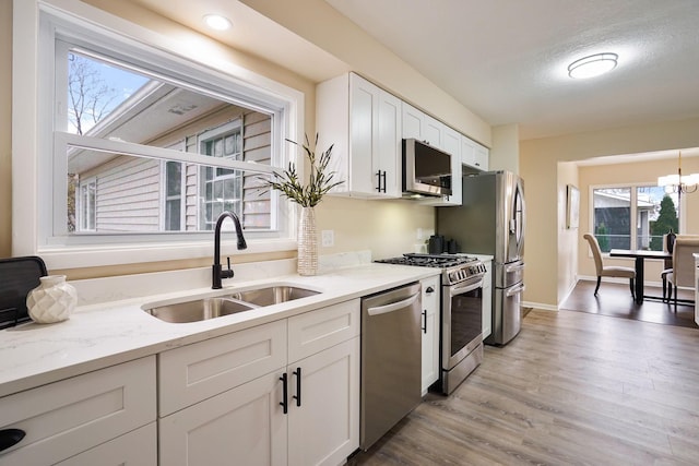 kitchen featuring light stone countertops, white cabinetry, sink, stainless steel appliances, and light wood-type flooring