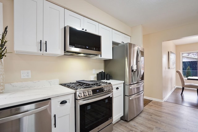 kitchen with white cabinets, light wood-type flooring, stainless steel appliances, and light stone counters