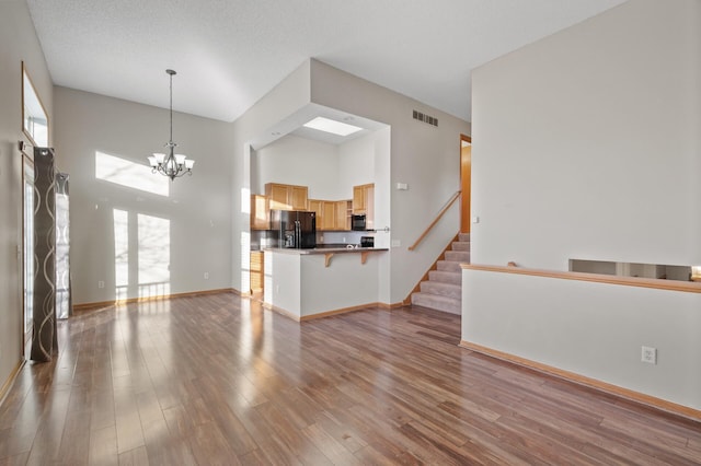 unfurnished living room with a high ceiling, a textured ceiling, light hardwood / wood-style flooring, and a notable chandelier