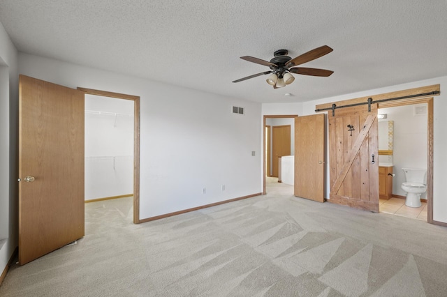 unfurnished bedroom featuring a walk in closet, light carpet, a barn door, and a closet