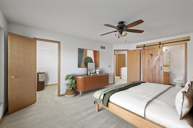 bedroom with ensuite bath, ceiling fan, a barn door, a spacious closet, and a closet