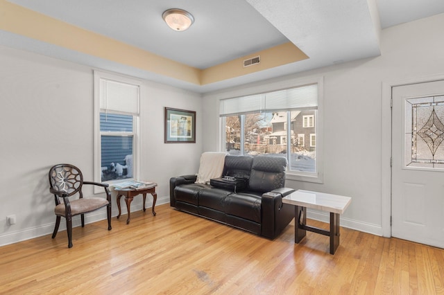 living area with a tray ceiling, light wood-style flooring, visible vents, and baseboards