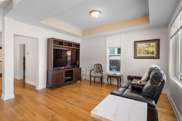 living room featuring a tray ceiling, light wood-style flooring, and baseboards