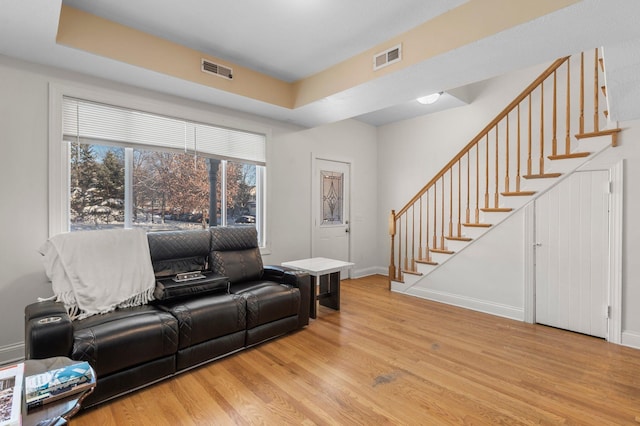 living room with light wood-style flooring, visible vents, stairway, and baseboards