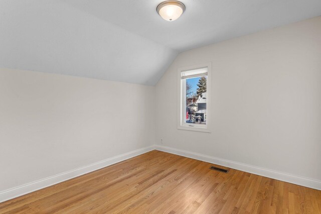 additional living space featuring light wood-type flooring, visible vents, lofted ceiling, and baseboards