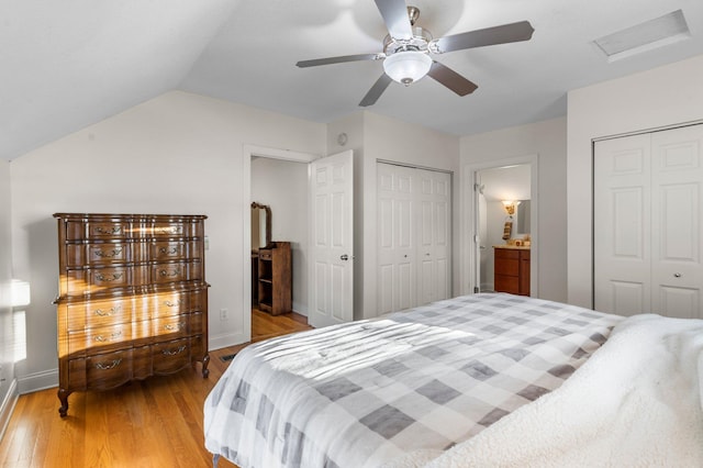 bedroom featuring light wood finished floors, attic access, a ceiling fan, lofted ceiling, and multiple closets