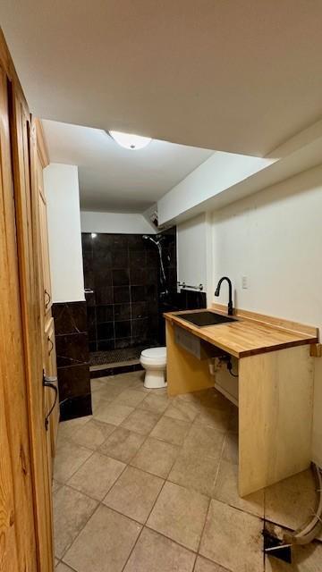 bathroom with tile patterned flooring, tiled shower, toilet, and sink